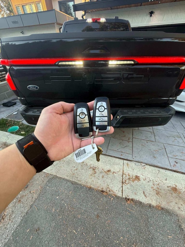 Hand holding two Ford key fobs behind a black Ford pickup truck