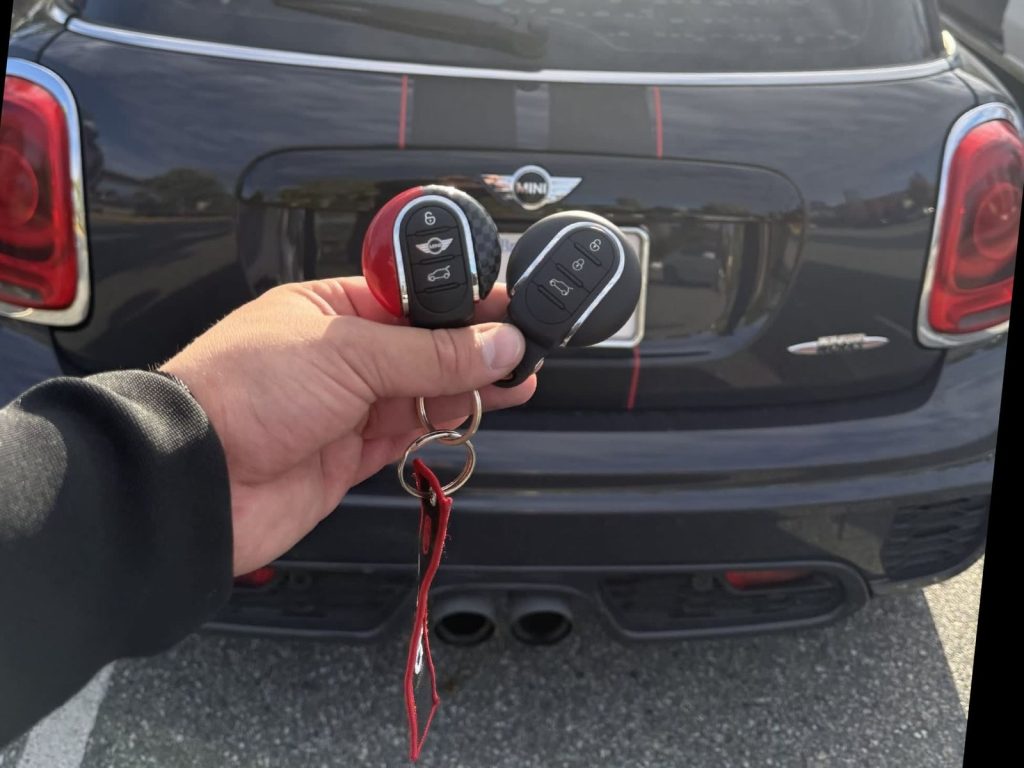 Two MINI key fobs held in front of the rear badge of a black MINI Cooper S