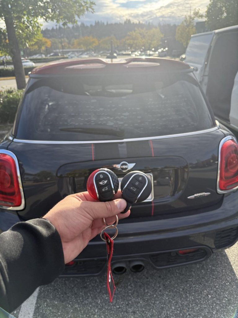 Hand holding two MINI key fobs behind a black MINI Cooper S parked outside