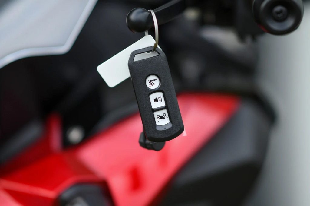 Motorcycle smart key fob with a tag held in front of a red motorcycle