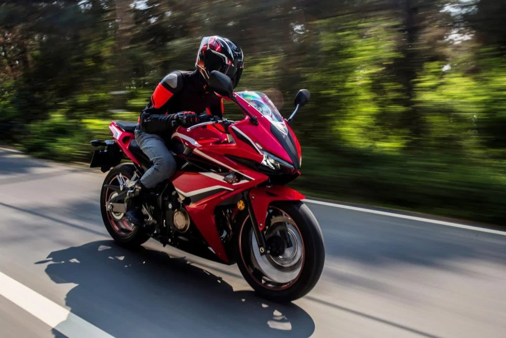 Rider on a red sport motorcycle on a tree-lined road