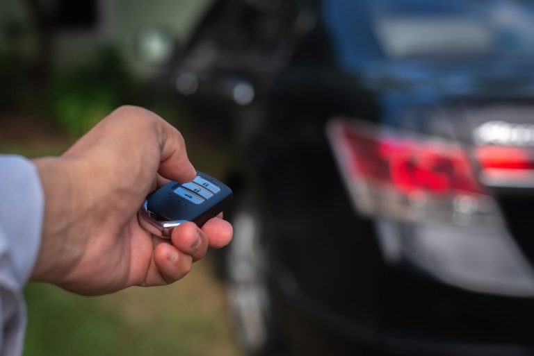 Hand holding a smart key fob beside the taillight of a black SUV