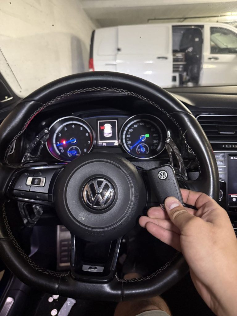 Hand holding a key fob over the steering wheel of a Volkswagen with the instrument cluster lit
