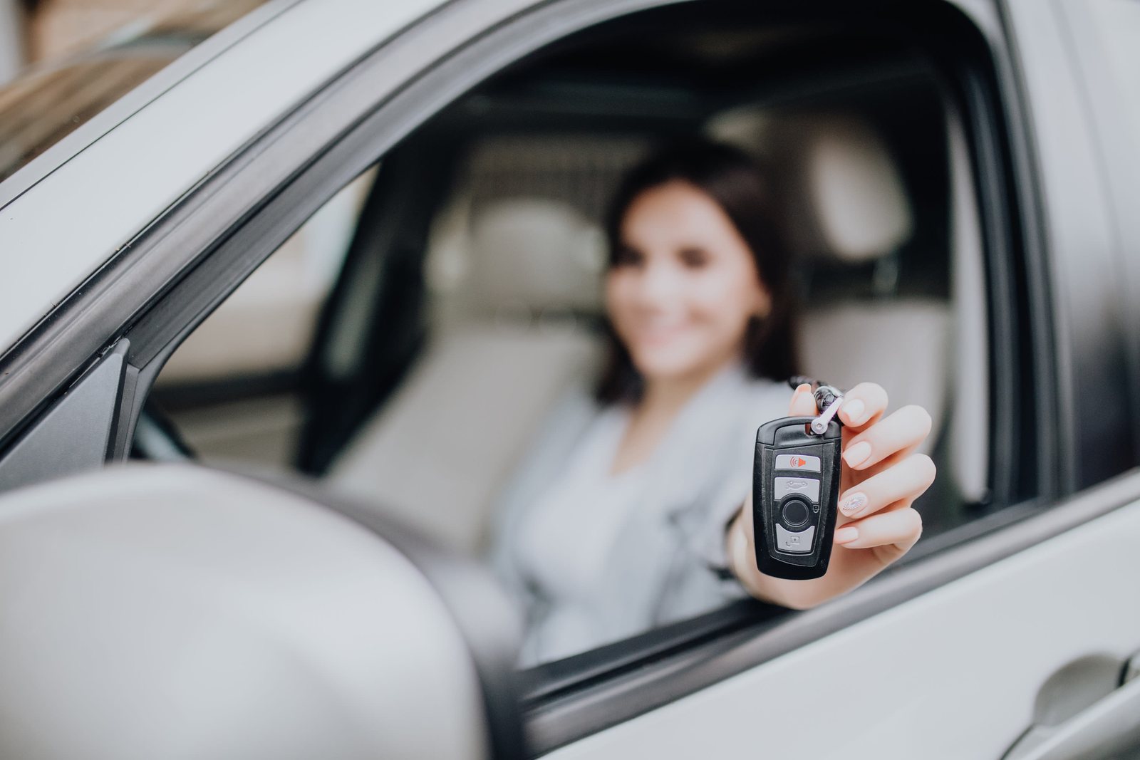 Smiling driver holding a smart key fob out of a car window